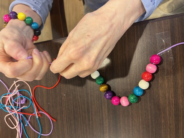 A resident and volunteer stringing a beaded bracelet together